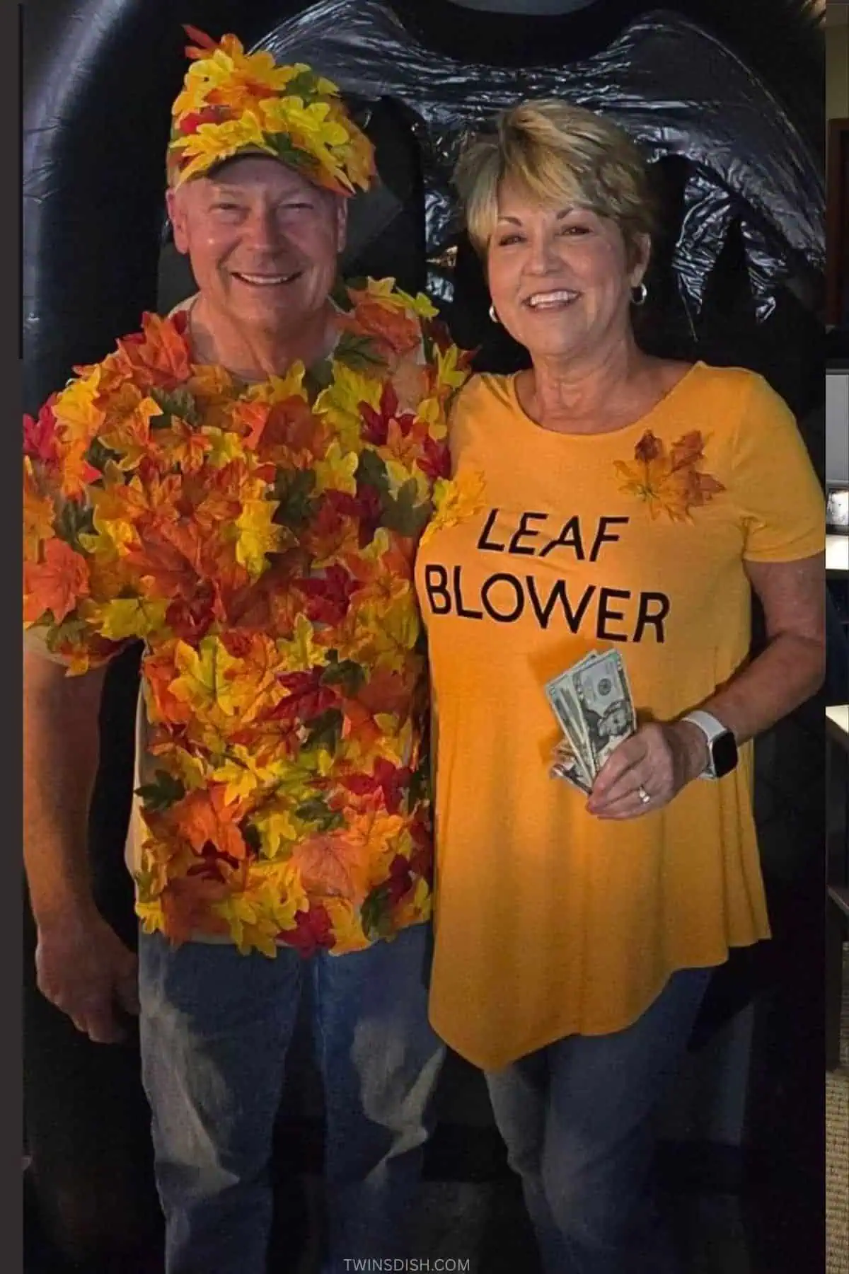 Couples Halloween costume featuring one person dressed in fall leaves and the other wearing a &ldquo;Leaf Blower&rdquo; shirt with money blowing around; a funny, easy DIY costume idea for parties or contests.